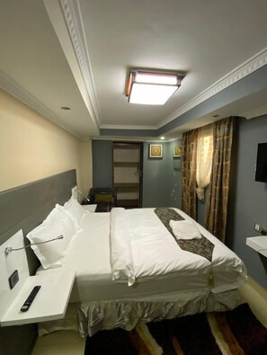 A hotel room with a large bed, a bedside table with a remote control, a flat-screen TV, and a window with curtains. - Ismarriot Hotel and Resort (Nairobi)