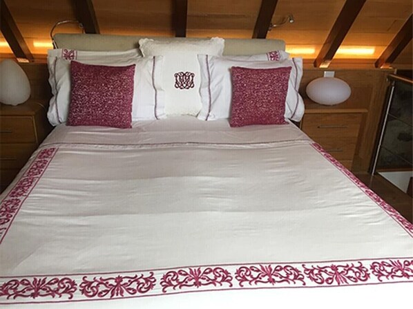 A bed with a white and pink bedspread, two pillows with pink and white patterns, and a wooden headboard.
