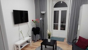 A living room with a TV, a small table, a bench, and a door leading outside. - D&N Hospedagem - Hostel (Lisbon)