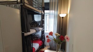 A narrow room with bunk beds, a small table with a vase of flowers, and a floor lamp. - D&N Hospedagem - Hostel (Lisbon)