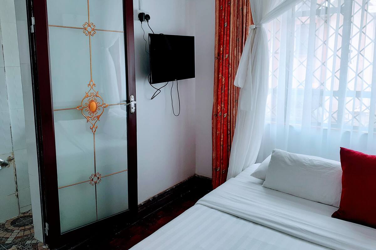 Ein Hotelzimmer mit Bett, Wandfernseher, dekorativer Tür und einem Fenster mit Vorhängen.