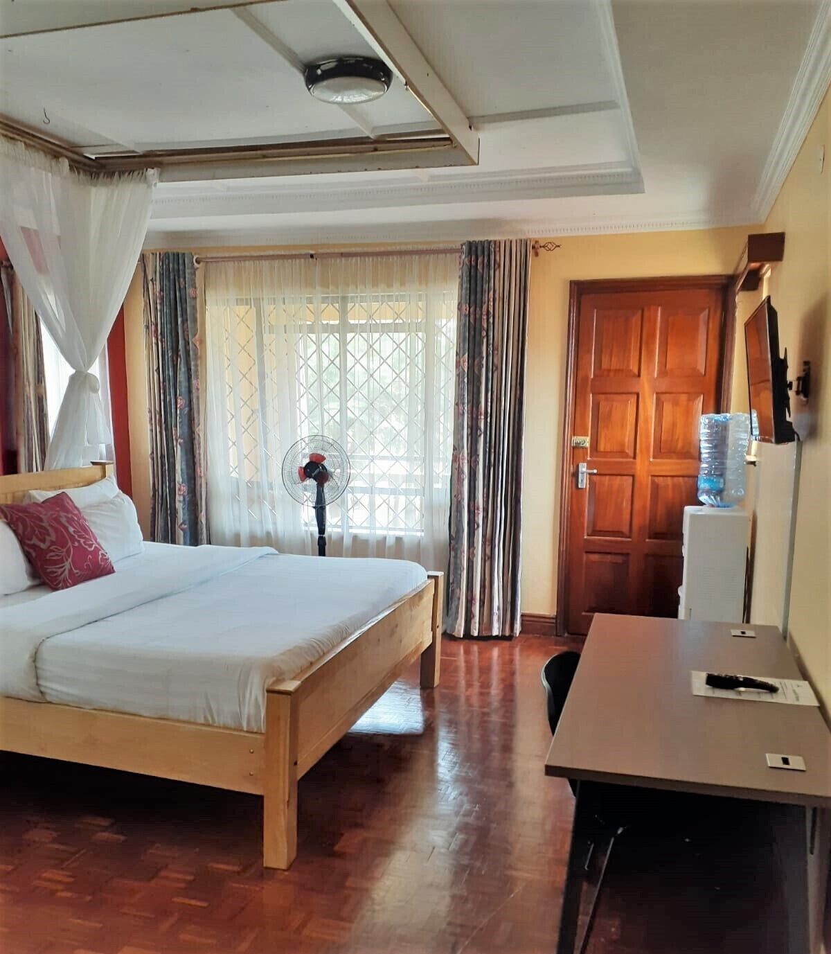 Un dormitorio con cama de madera, un escritorio, dispensador de agua y una ventana con cortinas.