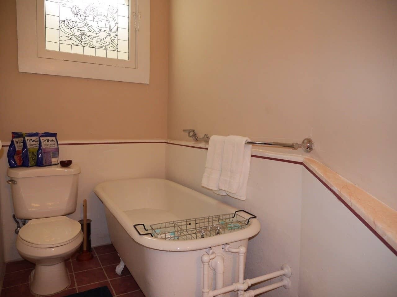 Un baño con inodoro, bañera y ventana con diseño de vitral.