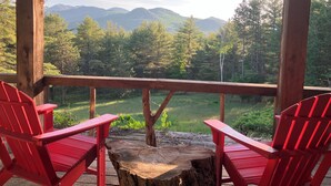 Una terraza de madera con dos sillas Adirondack rojas mirando una vista panorámica de montañas y árboles.
