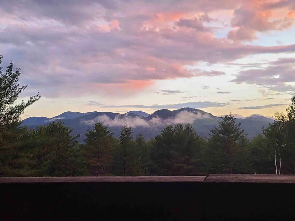 Un paysage montagneux, avec des arbres au premier plan et un ciel nuageux.