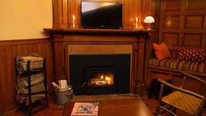 Una habitación acogedora con chimenea, un televisor montado sobre ella, una mesa de madera y una zona de estar cómoda con un sofá y una silla.