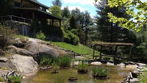 Un entorno r ústico al aire libre con un estanque, construcciones de madera y un edificio en el fondo.