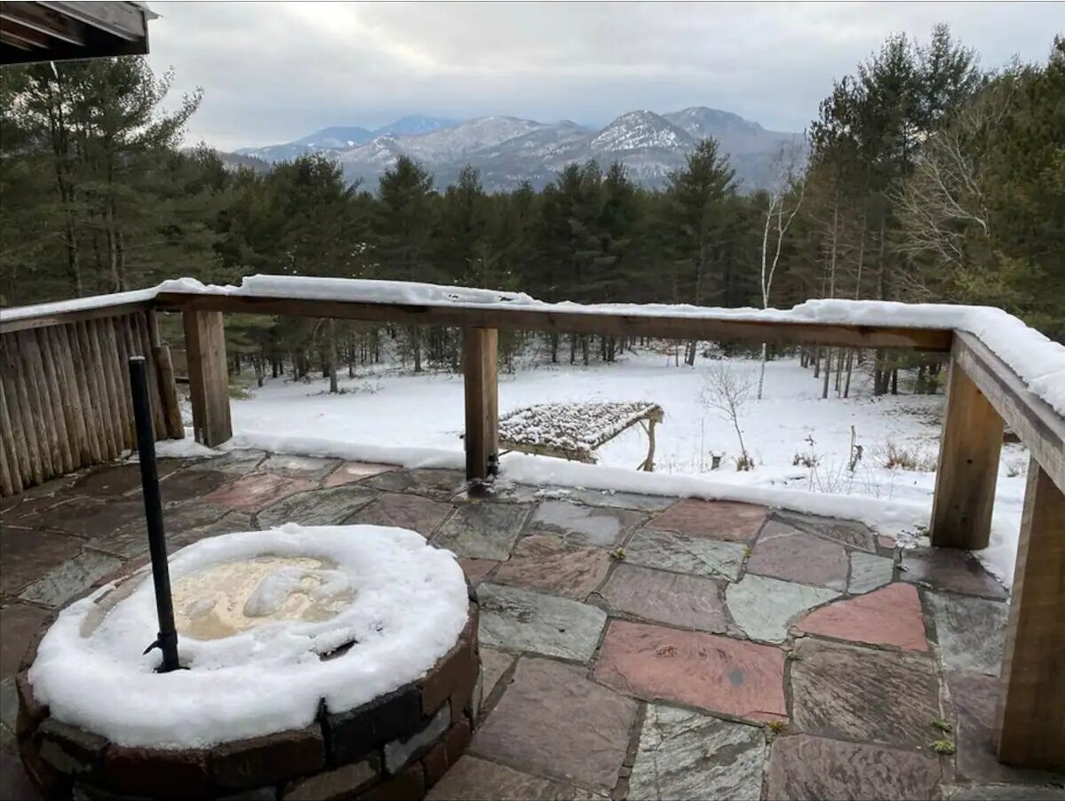 A stone deck with a snow-covered railing, a fire pit, and a view of snow-covered mountains.
