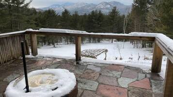 A stone deck with a snow-covered railing, a fire pit, and a view of snow-covered mountains.