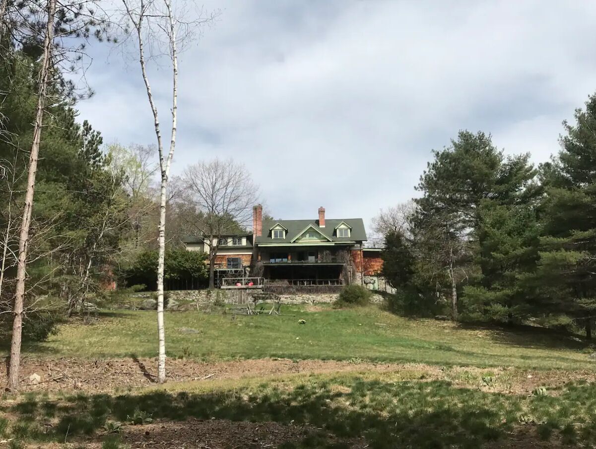 Une grande maison à deux étages, dotée d’un toit végétalisé et d’une façade en briques, entourée d’une pelouse et d’arbres.