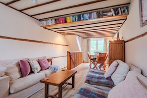 A cozy living room with a sofa, a wooden table, a patterned rug, and a bookshelf filled with books. - Charming, period cottage located just off the vibrant  high street of Deal with a gorgeous garden! (Deal)