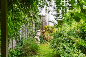 A garden with a statue, a wooden fence, and a white building in the background. - Charming, period cottage located just off the vibrant  high street of Deal with a gorgeous garden! (Deal)