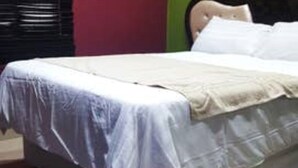 A bed with a white mattress and a beige blanket, a window with a black blind, and a green wall. - B & B - Pretoria La Vie (Booysens)