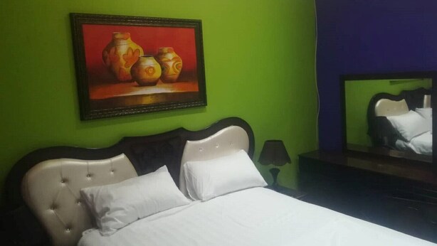 A bedroom with a bed, a painting of vases, a mirror, and a green wall. - B & B - Pretoria La Vie (Booysens)