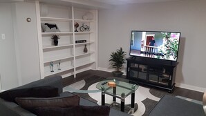 A living room with a television, a sofa, a glass coffee table, and a bookshelf. - The Filly - 6 miles to Churchill Downs - Pets - Highlands/Cherokee Triangle (Louisville)
