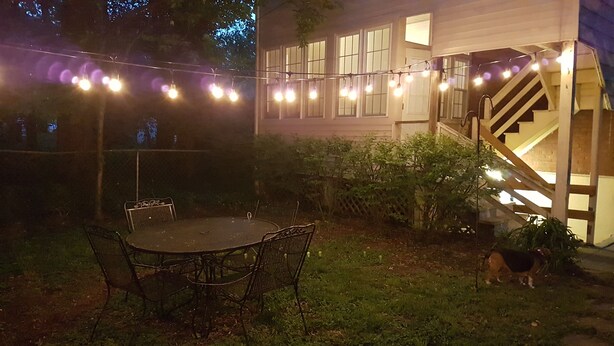 A backyard with a round metal table and chairs, a wooden staircase, and string lights. - The Filly - 6 miles to Churchill Downs - Pets - Highlands/Cherokee Triangle (Louisville)