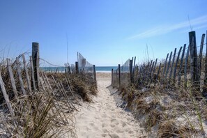 A sandy beach path leading to the ocean, bordered by wooden fences and dry grass.
