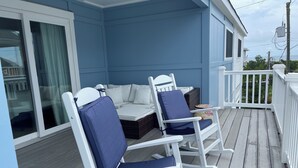 Un espace extérieur aménagé, abrité et doté de chaises berçantes blanches et d’une table, offrant une vue sur une étendue d’eau.