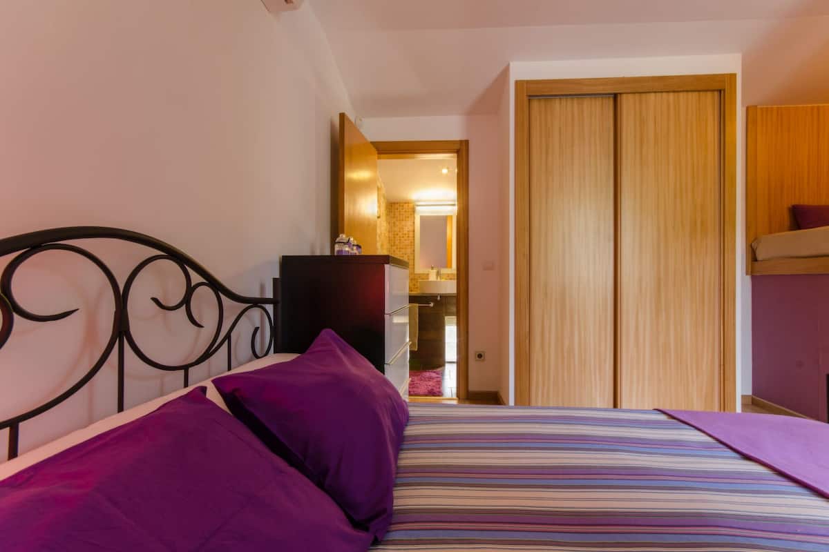 Un dormitorio con una cama, almohadas moradas, un aparador y un armario de madera.