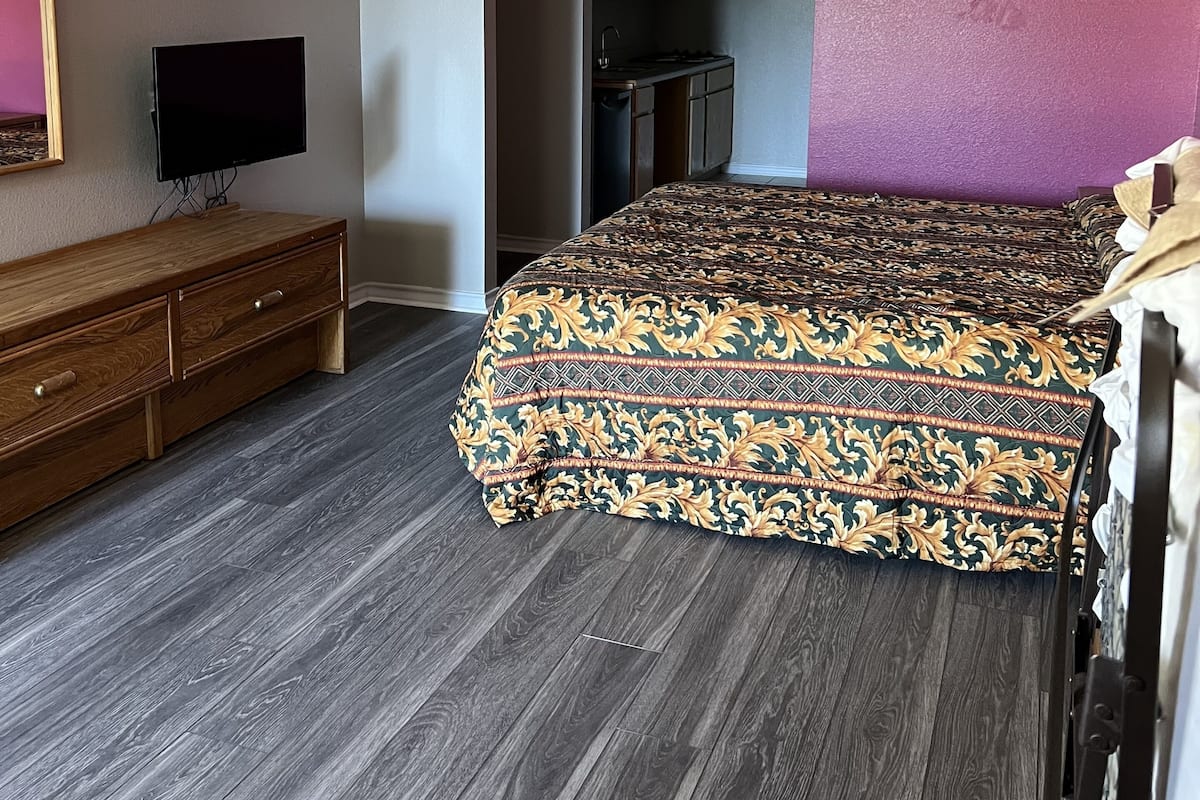 Una camera da letto con un letto, una cassettiera, una televisione e un angolo cottura.