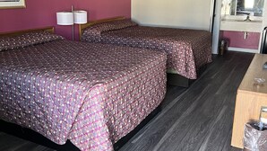 Quarto de hotel com duas camas, uma escrivaninha de madeira, um espelho e um cesto de lixo.
