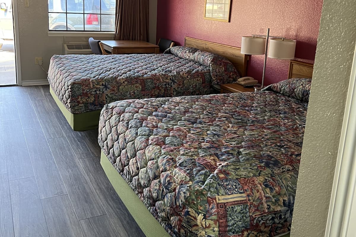 Una camera d'albergo con due letti, una finestra con tende, una scrivania e una sedia.