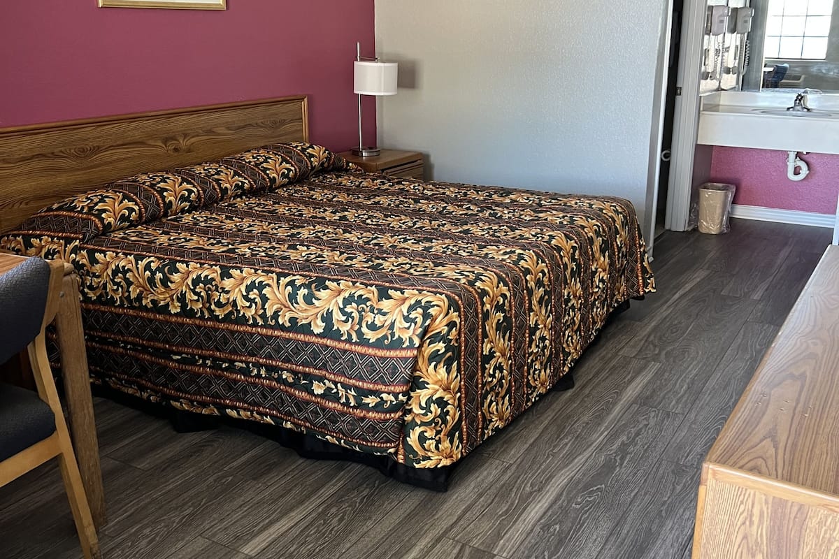 Camera d'albergo con un letto grande, un comodino in legno, una scrivania e un bagno con lavandino e specchio.