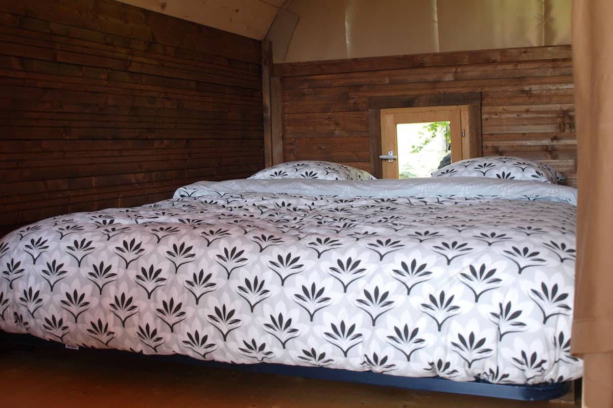 A wooden cabin bedroom with a bed, a wooden door, and a view of greenery outside.