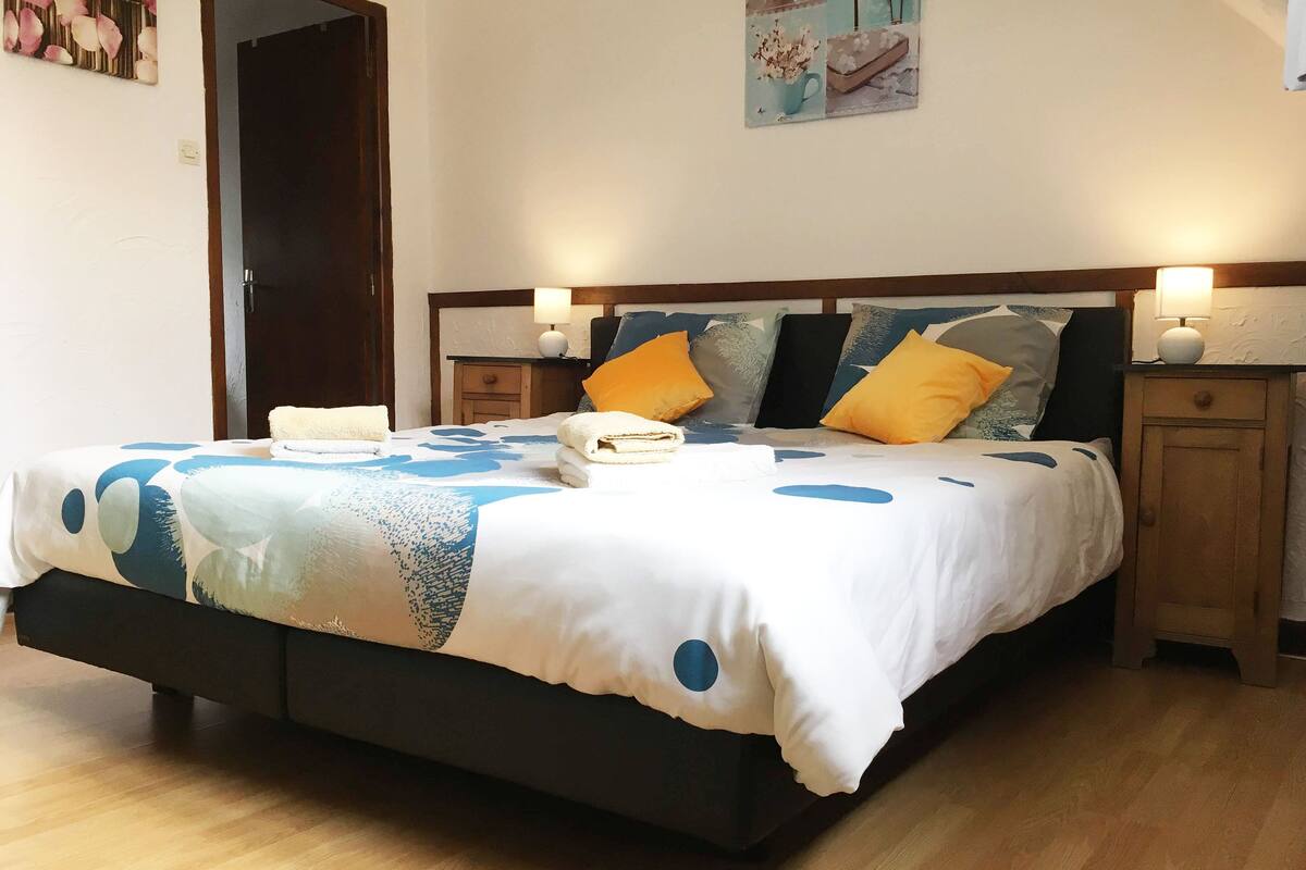 A neatly made bed with a patterned bedspread, two bedside tables with lamps, and a door in the background.