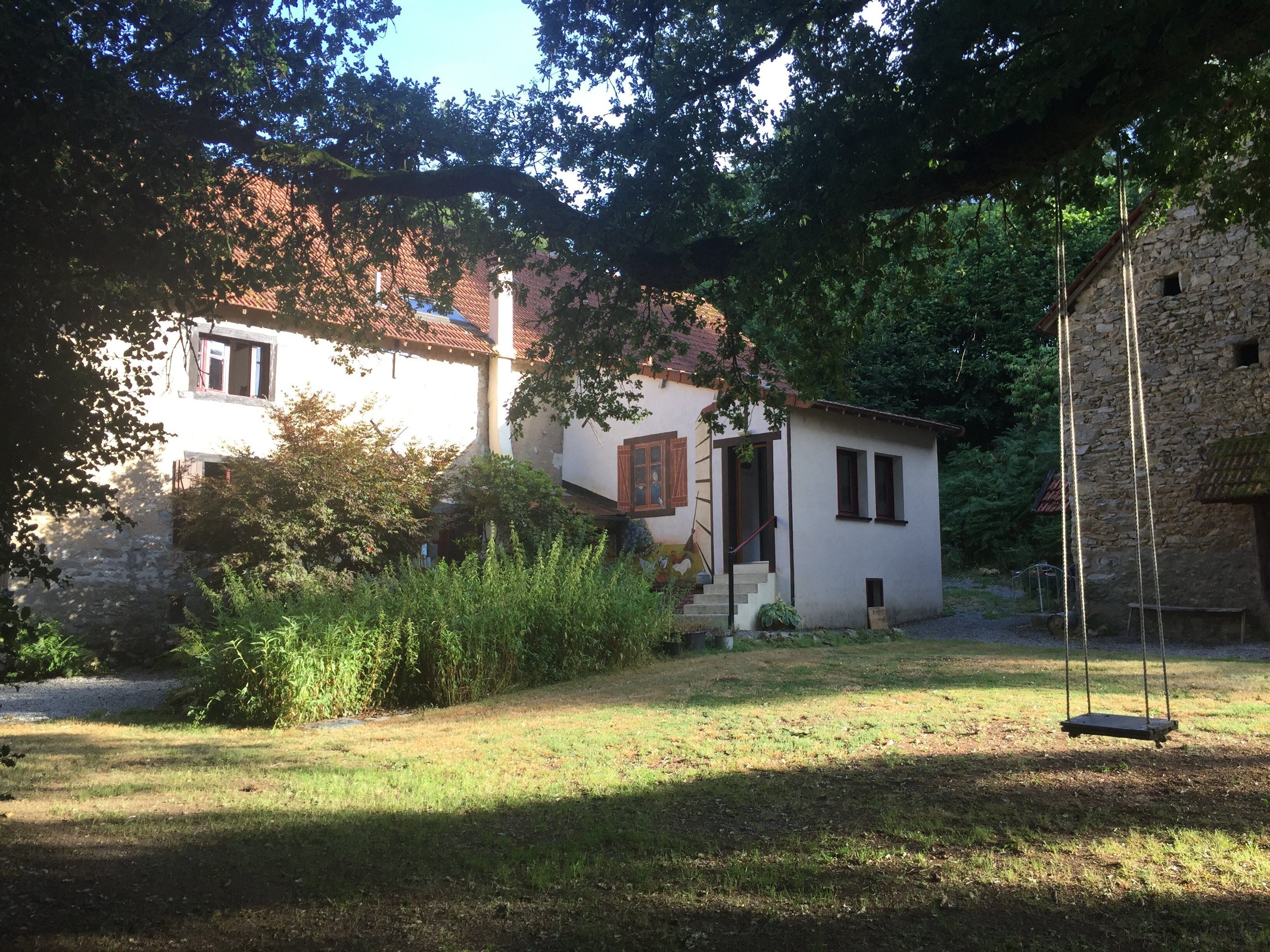 A rustic stone building with a small porch and a swing set in a garden.