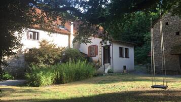 A rustic stone building with a small porch and a swing set in a garden.