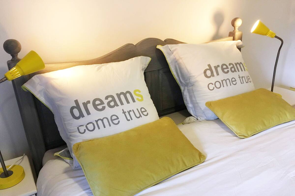 A bed with two pillows that read "dreams come true" and a bedside lamp.