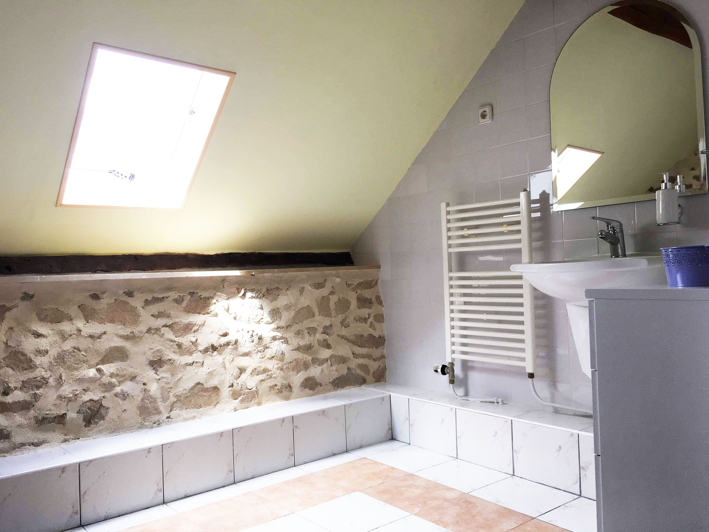 A bathroom with a stone wall, a bathtub, a white sink, and a skylight.