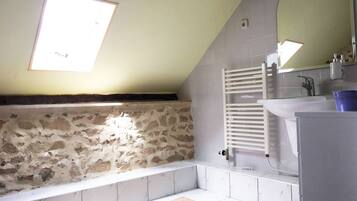 A bathroom with a stone wall, a bathtub, a white sink, and a skylight.