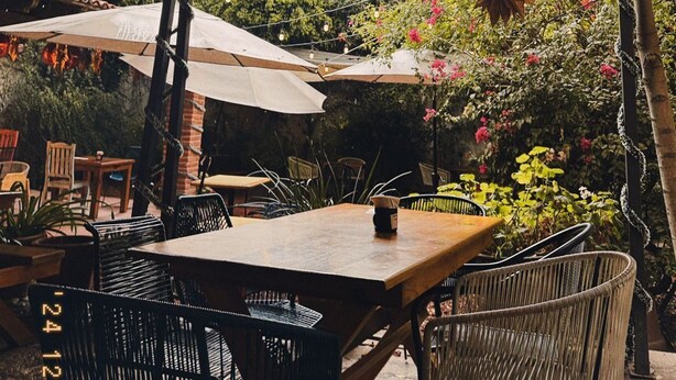 Un patio al aire libre con una mesa y sillas de madera, rodeado de sombrillas y luces colgantes.