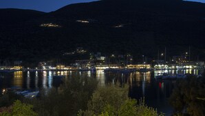 A nighttime view of a coastal town with buildings along the waterfront, boats docked at the marina, and a hill in the background.