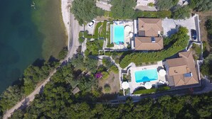 An aerial view of a coastal property with two swimming pools, a beach, and lush greenery.