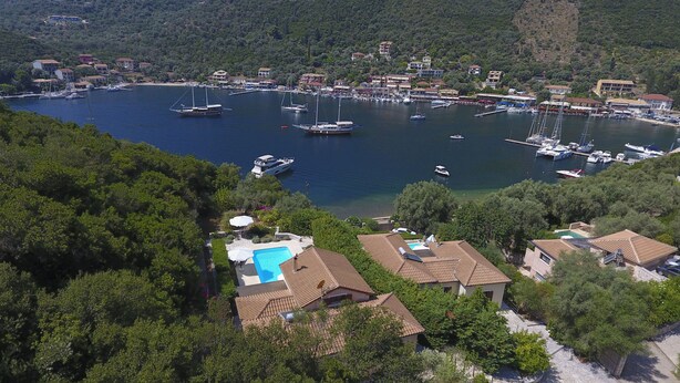 An aerial view of a coastal town with a marina, houses with tiled roofs, and a swimming pool.