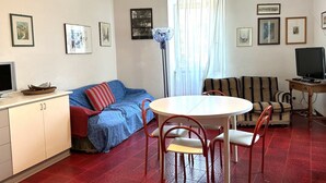 Ein Wohnzimmer mit einer Couch, einem Esstisch mit Stühlen, einem Fernseher und Bildern an den Wänden.