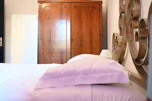 A bedroom with a wooden wardrobe, a bed with white bedding, and a decorative wall piece.