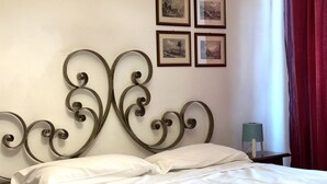 Ein Bett mit Metallkopfteil, weißer Bettwäsche und einem Nachttisch mit Lampe.