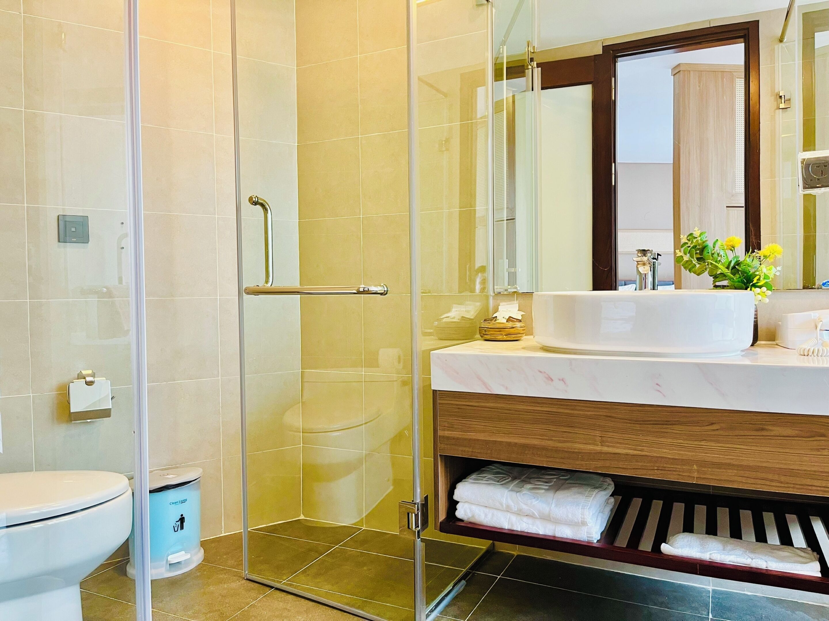A modern bathroom with a glass shower enclosure, a white sink with a marble countertop, and a wooden vanity.