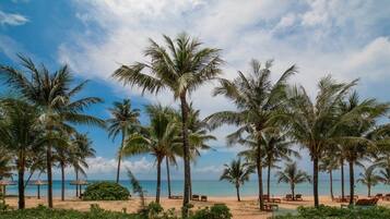A beach with palm trees, a thatched-roof hut, and beach chairs.