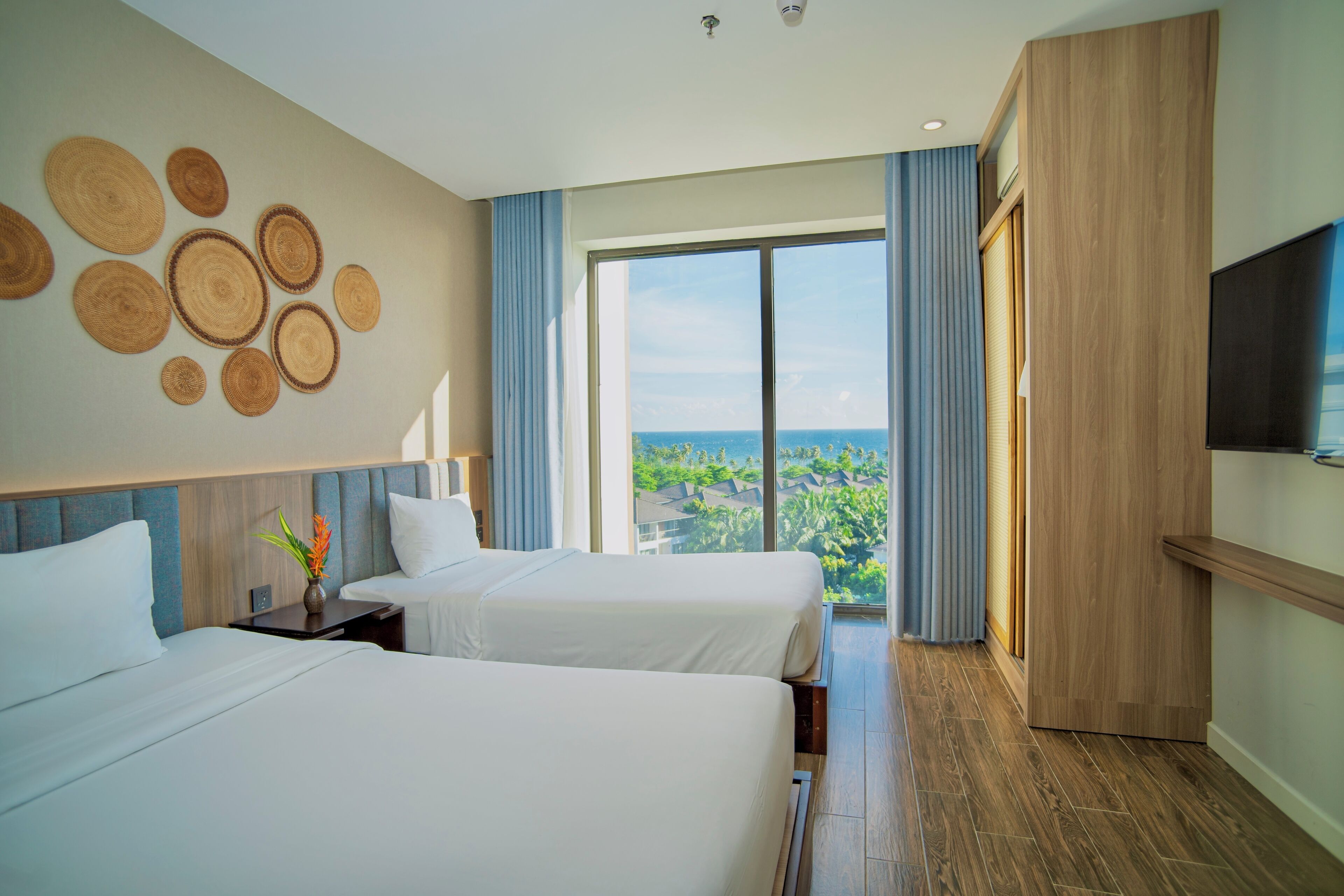 Une chambre d’hôtel avec deux lits, une grande fenêtre donnant sur la ville, un téléviseur à écran plat et une armoire en bois.