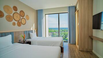 Une chambre d’hôtel avec deux lits, une grande fenêtre donnant sur la ville, un téléviseur à écran plat et une armoire en bois.
