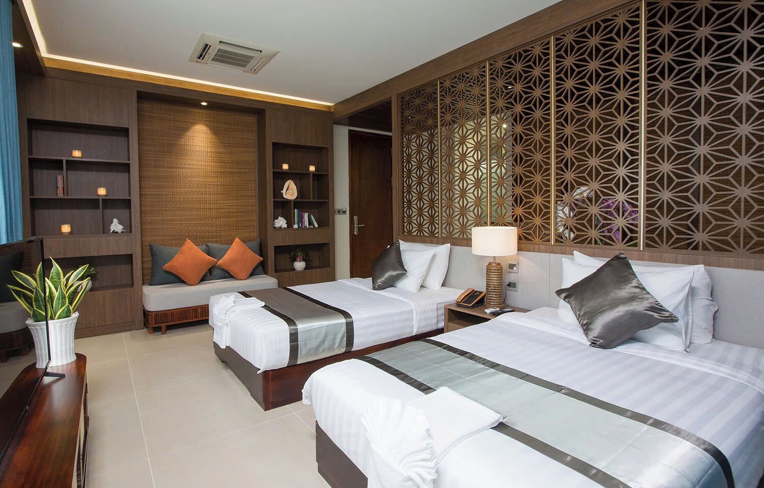 Habitación de hotel con dos camas, un sofá, un televisor, una estantería y un panel decorativo en la pared.