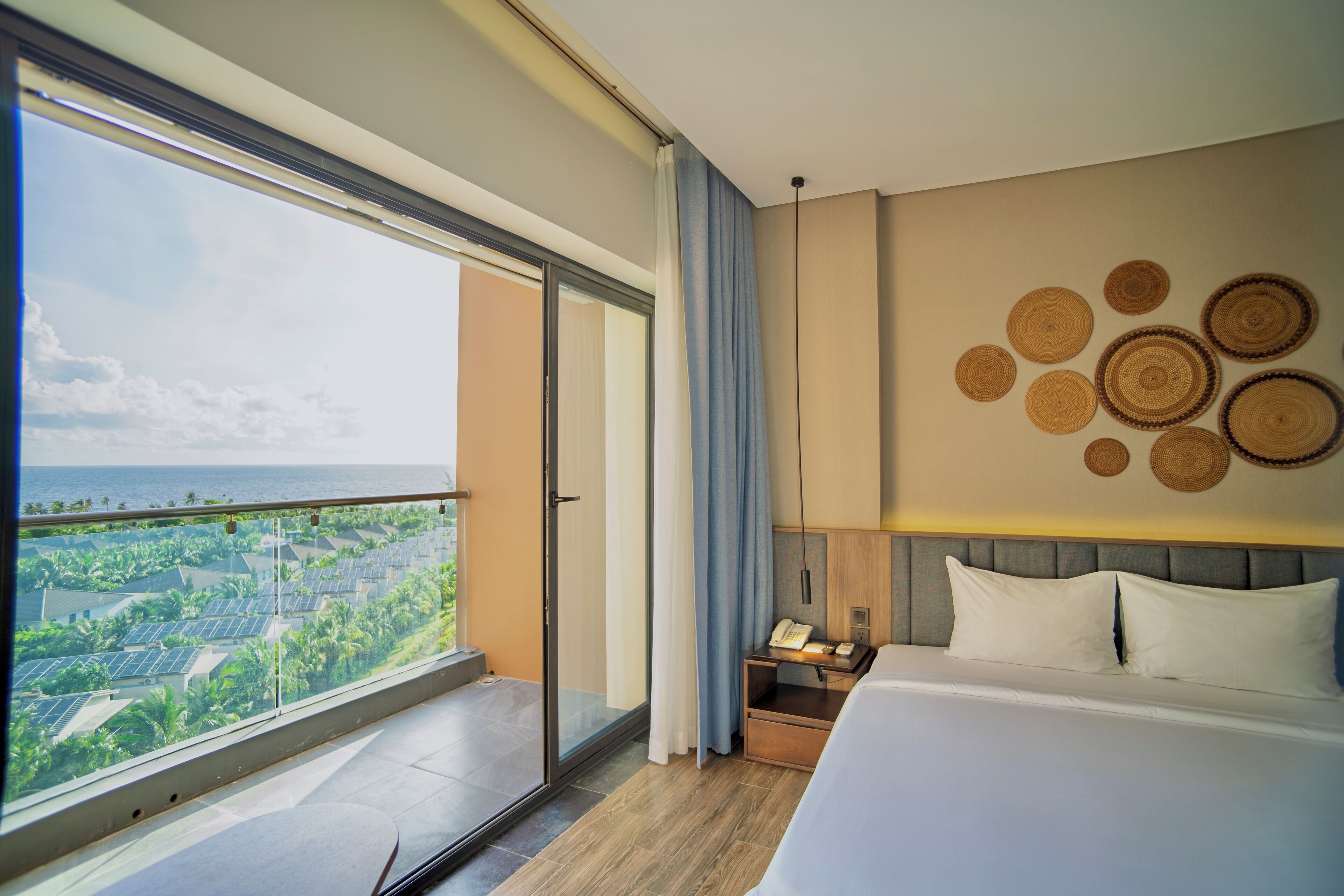 Ein Hotelzimmer mit großem Fenster, einem Bett, einem Nachttisch und einer Wand mit runder Wandkunst.