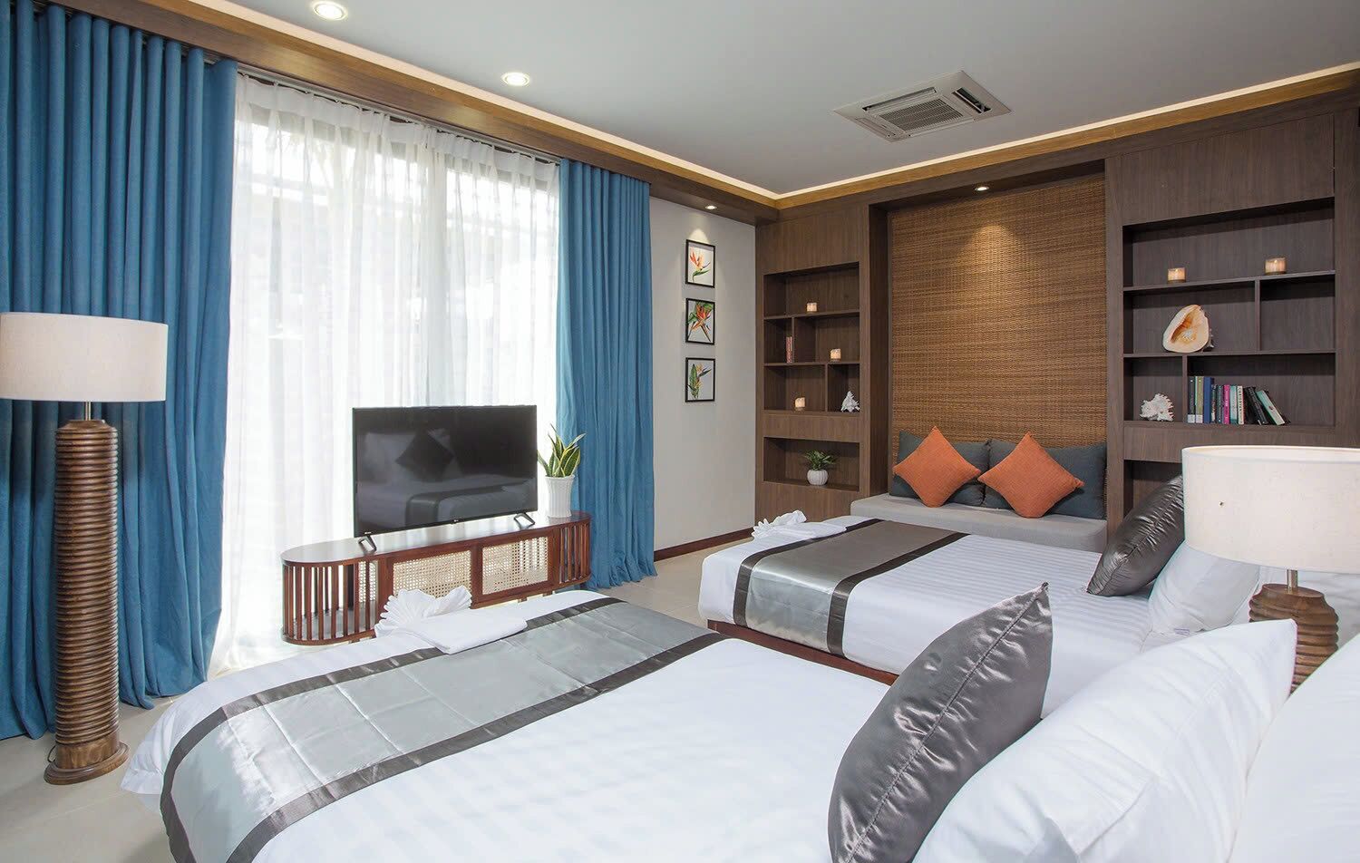 A hotel room with two beds, a TV, a bookshelf, and a large window with curtains.