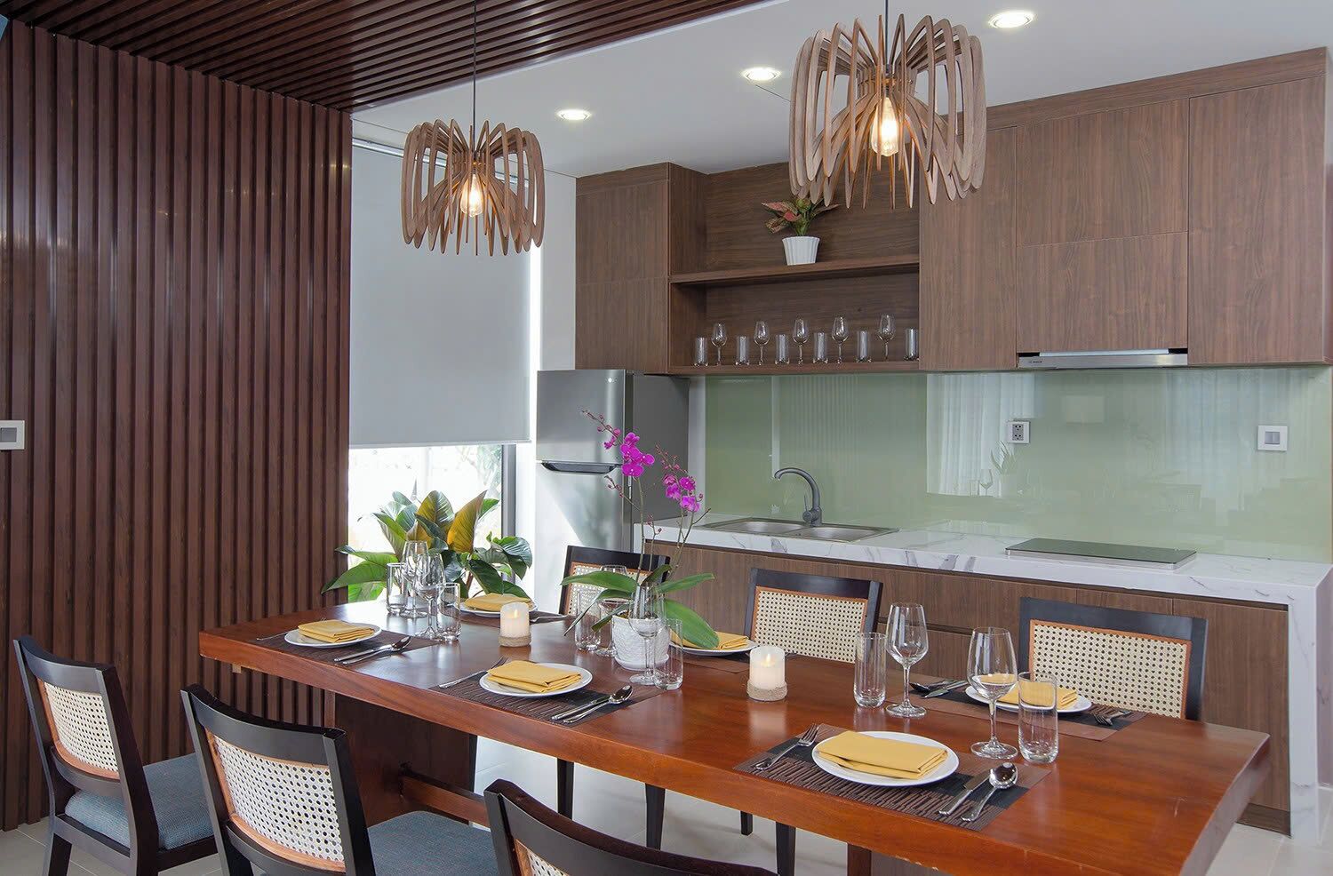 A modern kitchen with wooden cabinets, a marble countertop, and a dining area set with a wooden table and chairs.