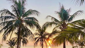 A beach scene with palm trees, a sunset, and two wooden chairs. - Sonaga Beach Resort & Villas Phu Quoc (Phu Quoc)